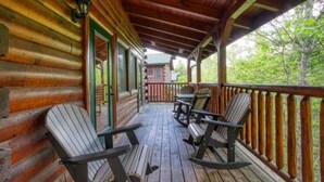 A wooden cabin with a covered porch, rocking chairs, and a view of the surrounding forest.