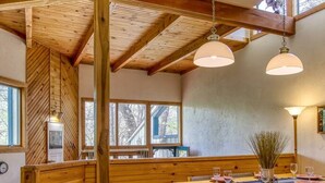 Un intérieur en bois comprenant un coin repas, des poutres apparentes et de grandes fenêtres.