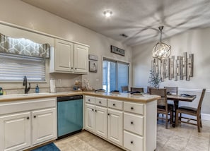 A kitchen with white cabinets, a dishwasher, a dining area with a wooden table and chairs, and a 'WELCOME' sign on the wall. - Irresistible Retreat w Pool Hot Tub Arcade (Sevierville)