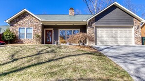 A two-story house with a stone facade, a garage, and a well-maintained lawn. - Irresistible Retreat w Pool Hot Tub Arcade (Sevierville)