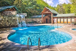 Una piscina con cascada, sillas de descanso y una estructura tipo cabaña de madera.