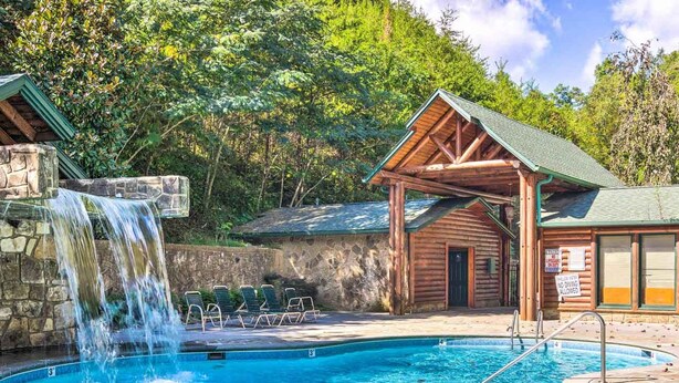 A swimming pool with a waterfall feature, lounge chairs, and a wooden cabin structure. - Dog Friendly Romantic Mtn Getaway Hot Tub Pool (Gatlinburg)