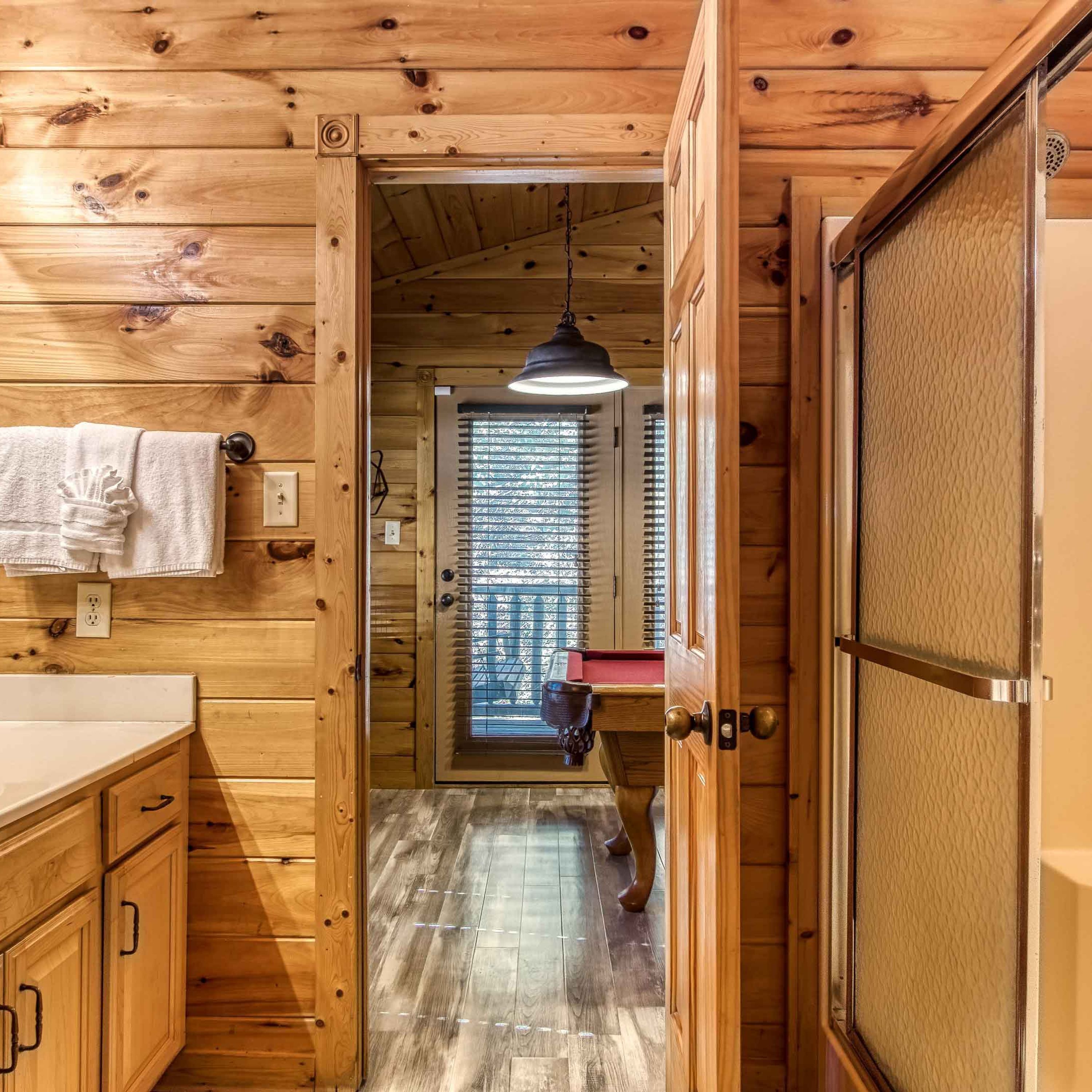 A wooden interior with a kitchen area, a hallway leading to a room with a window, and a door with a textured panel.