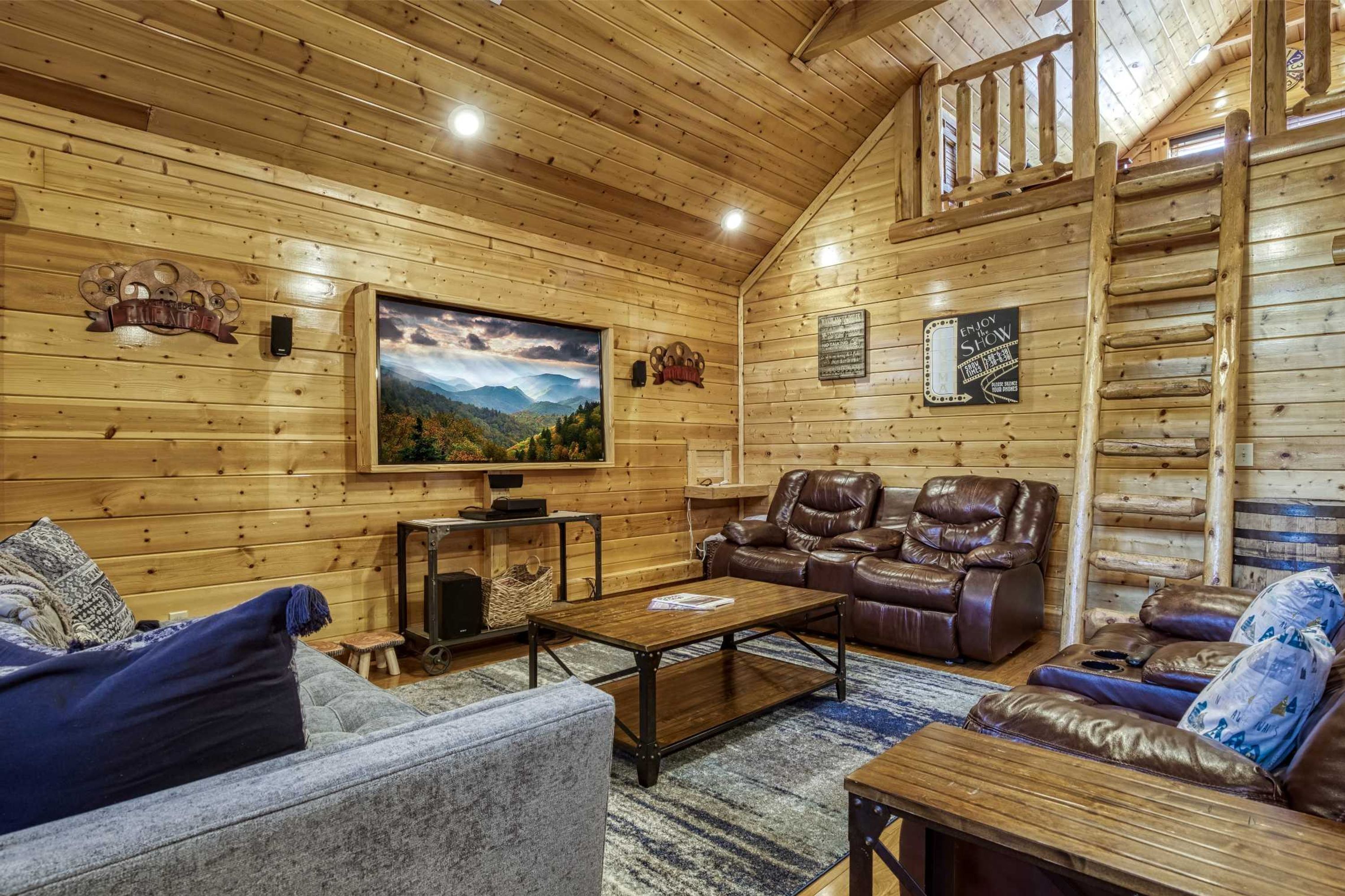 L’intérieur d’un chalet confortable, avec une grande télévision, des fauteuils inclinables en cuir et un escalier en bois.