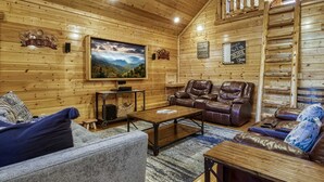 Ein gemütliches Blockhaus-Interieur mit einem großen Fernseher, Ledersessel und einer Holztreppe.