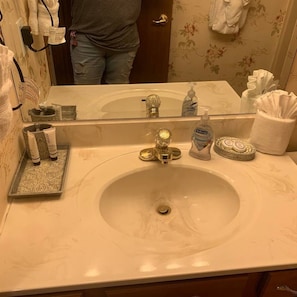A bathroom with a marble sink, a mirror, toiletries, and a towel rack.