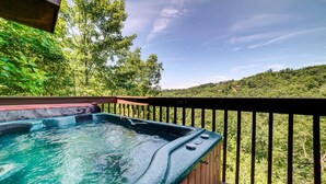 Ein Whirlpool auf einer Holzterrasse mit Blick auf einen bewaldeten Hang.