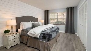 Una camera da letto con un letto, un comodino, una lampada e una finestra con tende.