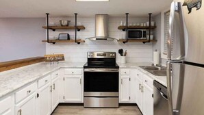Una cucina moderna con mobili bianchi, elettrodomestici in acciaio inossidabile e mensole in legno.