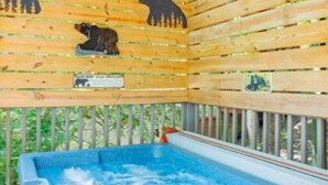 Una cabaña de madera con hidromasaje, paredes de madera con siluetas de osos y vistas a la vegetación.