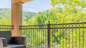A balcony with wicker furniture and a metal railing overlooking a forested area. - Luxurious Condo Pool Fireplace Hiking (Gatlinburg)