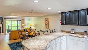 A modern kitchen with white cabinets, granite countertops, and a dining area with a yellow sofa and metal chairs. - Luxurious Condo Pool Fireplace Hiking (Gatlinburg)