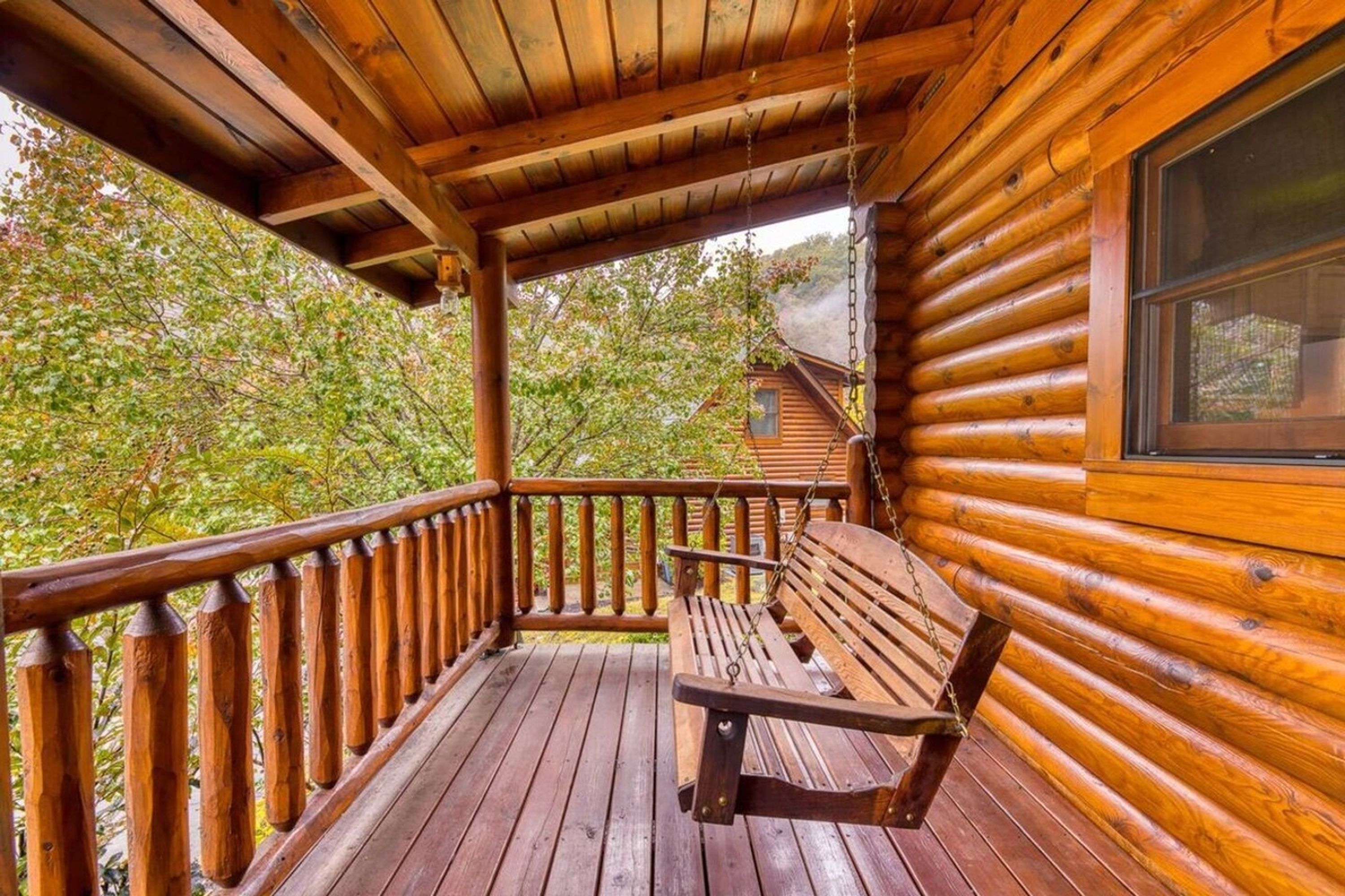 A wooden cabin with a porch, a swing, and a window overlooking a forested area.