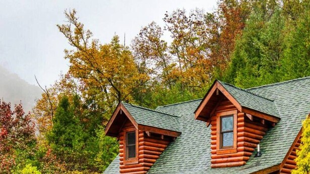 A log cabin with a porch and two dormer windows, surrounded by dense forest. - Cozy Upscale Cabin w Fireplace Hot Tub (Sevierville)