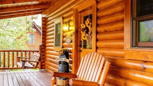 A wooden cabin with a porch, rocking chairs, and a glass table. - Cozy Upscale Cabin w Fireplace Hot Tub (Sevierville)