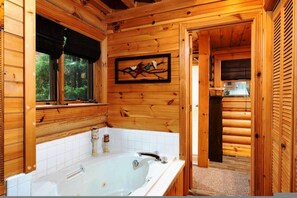 Baño de cabaña de madera con una bañera grande, una ventana con vista a árboles y una obra de arte enmarcada en la pared.