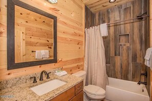 A wooden cabin bathroom with a granite countertop sink, a mirror, a toilet, and a bathtub. - Private Pool Home Theater Game Room Phenomenal Views (Sevierville)
