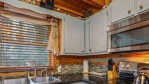 A kitchen with white cabinets, a stainless steel sink, and a stove. - A Charming Cabin Pool Firepit Hot Tub-jacuzzi (Gatlinburg)