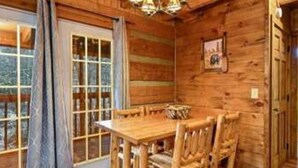 A wooden interior with a dining table and chairs, a chandelier, and a door leading outside. - A Charming Cabin Pool Firepit Hot Tub-jacuzzi (Gatlinburg)