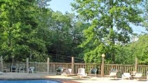 A swimming pool with a wooden deck, lounge chairs, and a fence. - A Charming Cabin Pool Firepit Hot Tub-jacuzzi (Gatlinburg)