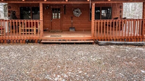 A wooden cabin with a green roof, a porch with railings, and a front door. - A Charming Cabin Pool Firepit Hot Tub-jacuzzi (Gatlinburg)
