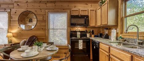 A wooden cabin interior with a dining area, kitchen, and large windows.