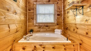 Une salle de bain rustique, avec des murs en bois, une grande baignoire, une fenêtre et une étagère sur laquelle est posé un vase.