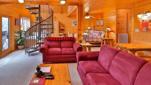 Interior acogedor de una cabaña de troncos con una escalera de caracol, dos sofás rojos, una mesa de centro de madera y una mesa de comedor.
