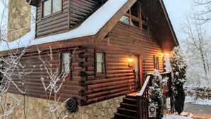 Una cabaña de troncos con cimientos de piedra, una chimenea y un techo cubierto de nieve.