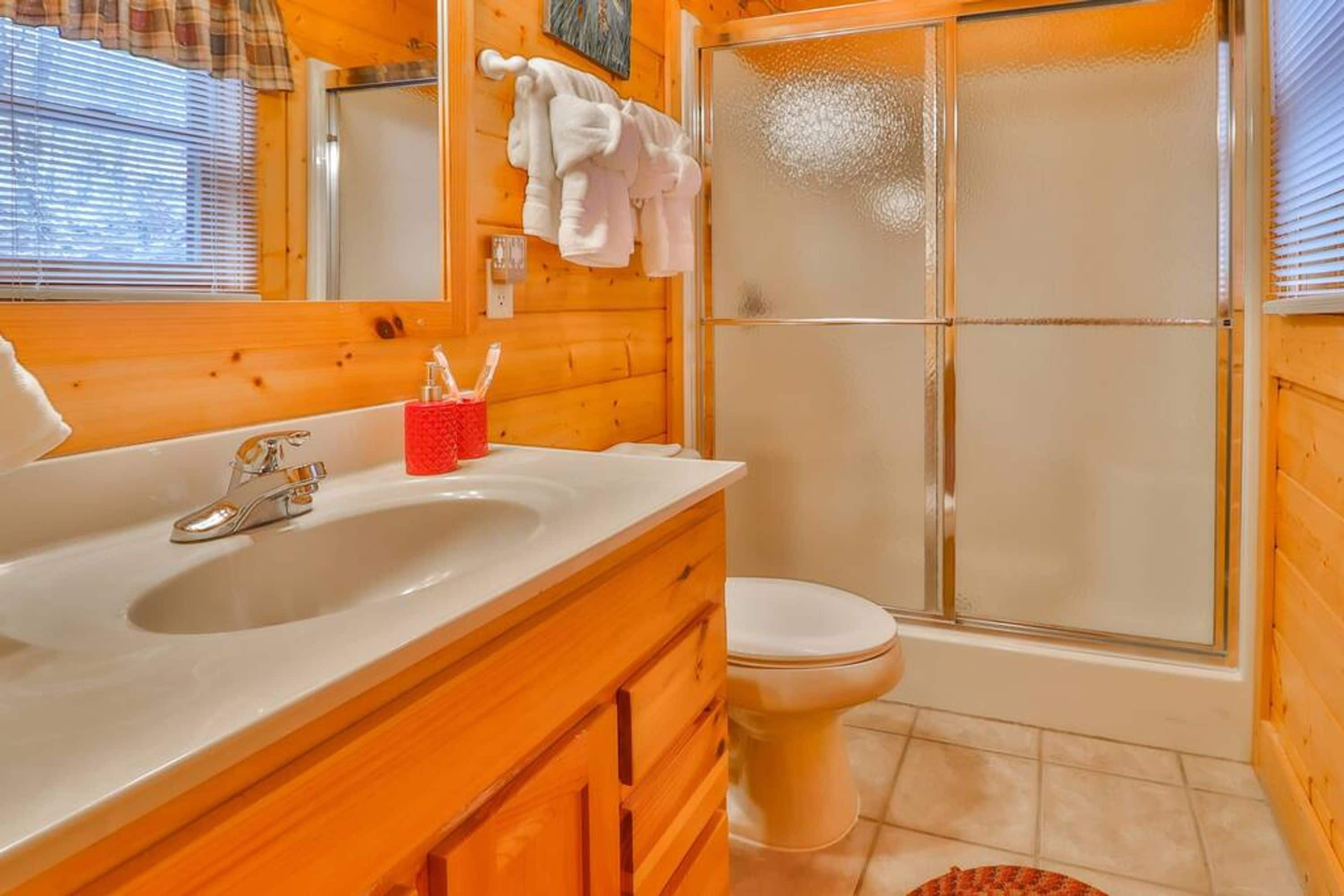 A bathroom with a wooden vanity, a sink, a toilet, and a glass shower enclosure.