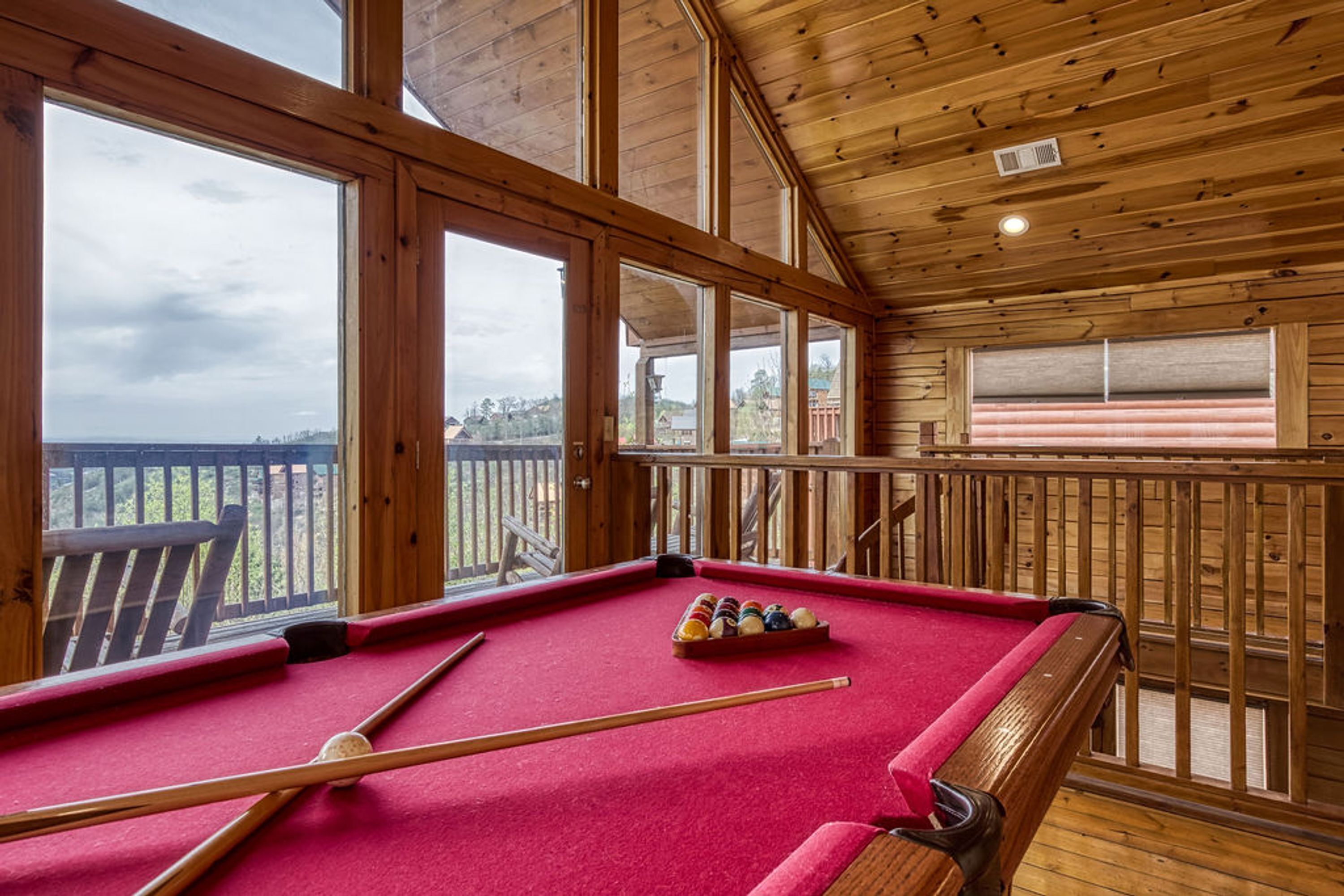 A pool table in a wooden room with large windows and a view of the outdoors.