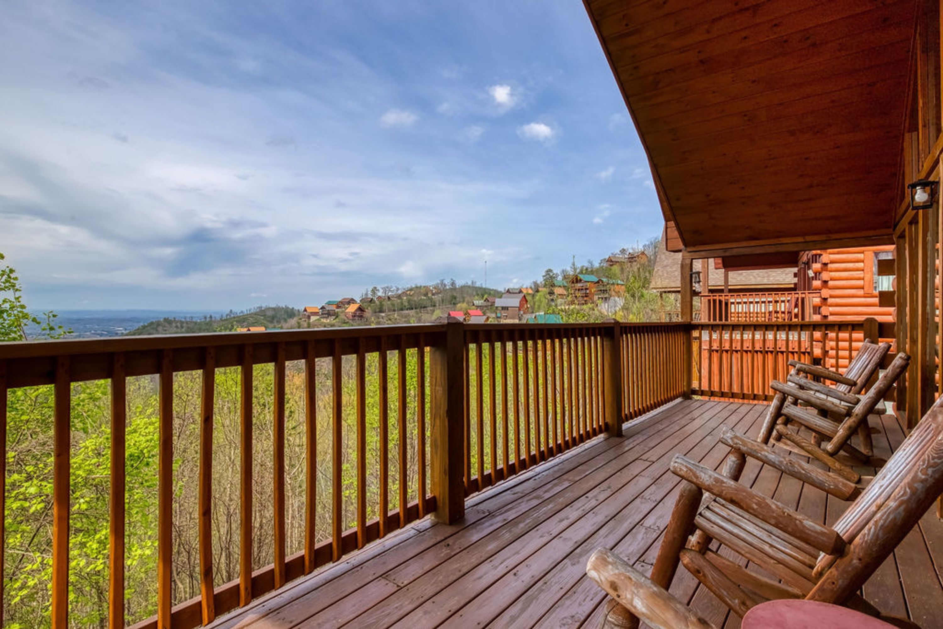 Een houten terras met een balustrade, met uitzicht op een bebost gebied en verre heuvels.