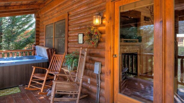 Una cabaña de madera con porche cubierto, mecedoras y jacuzzi.