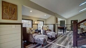 A spacious room with two armchairs, a wooden floor, and a staircase. - New Luxury Remodel Fire Pit Game Room Hot Tub (Sevierville)
