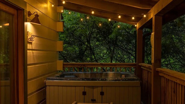 A wooden deck with a hot tub, string lights, and a view of trees.