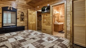 A wooden cabin bedroom with a bed, a television, a mirror, a bathroom with a sink, and a wardrobe.