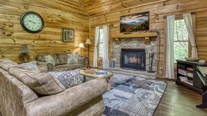 A cozy log cabin interior with a stone fireplace, leather sofas, and a large clock on the wall.