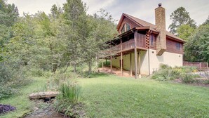 A rustic cabin with a stone chimney, wooden deck, and a small stream in the yard. - 5-star w Pool Cozy Secluded Newly-renovated (Sevierville)