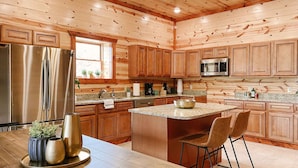 A modern kitchen with wooden cabinetry, stainless steel appliances, granite countertops, and a central island with bar stools. - Modern Luxury w Pool Theater Hot Tub Ent Room (Sevierville)