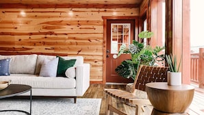 A cozy living room with a wooden wall, a sofa with cushions, a coffee table, a chair, and a large potted plant. - Modern Luxury w Pool Theater Hot Tub Ent Room (Sevierville)