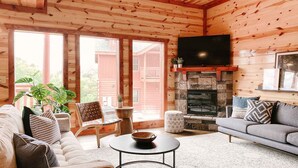 A cozy log cabin interior with a stone fireplace, a flat-screen TV mounted above it, and a comfortable seating area with a sofa and chairs. - Modern Luxury w Pool Theater Hot Tub Ent Room (Sevierville)