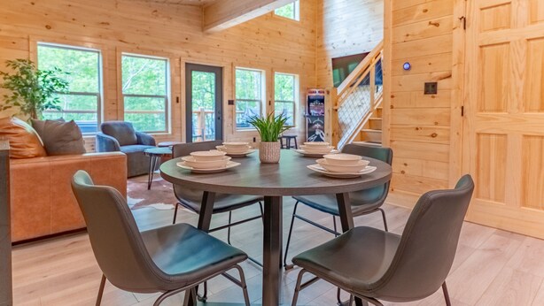 A wooden cabin interior with a dining area, a sofa, and a staircase. - Brand New 2 bed 2 Bath Arcade Games Hot Tub (Sevierville)