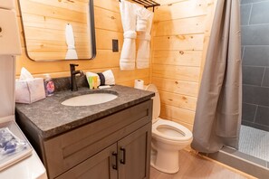 Ein Badezimmer einer Holzhütte mit einem Granitwaschbecken, einer Toilette und einer Dusche.