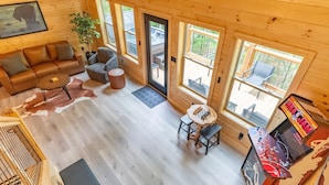 A wooden cabin interior with a sofa, armchair, coffee table, and a foosball table. - Brand New 2 bed 2 Bath Arcade Games Hot Tub (Sevierville)