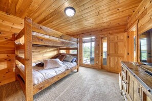 A wooden cabin interior with a bunk bed, a wooden cabinet, and a door leading outside. - Awe-inspiring Estate w Pool Theater Fire Pit (Pigeon Forge)