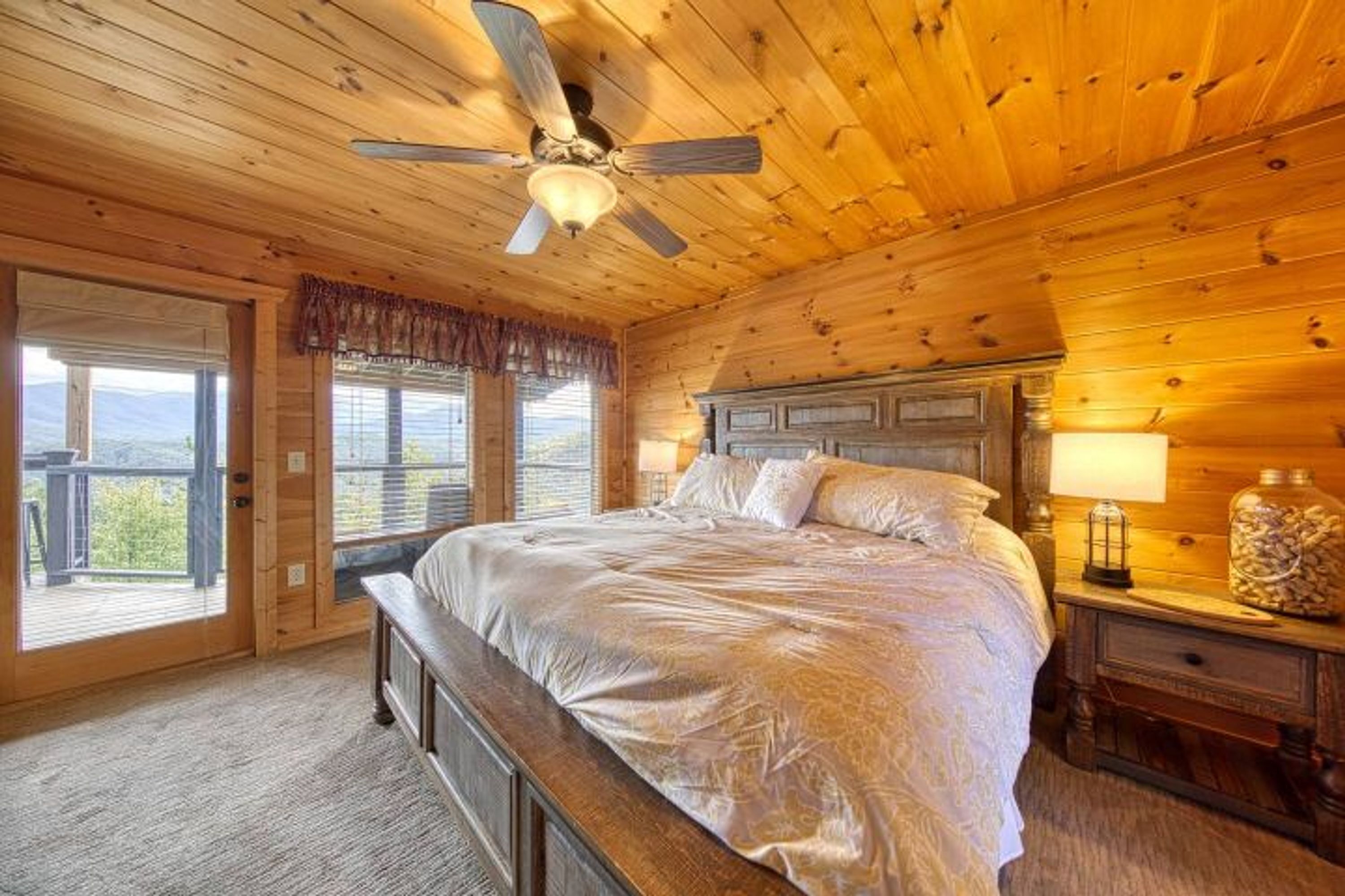 A bedroom with a wooden ceiling, a large bed, a nightstand, and a window with a view.