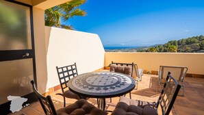 Eine Terrasse mit einem runden Tisch und Stühlen, Blick auf die Landschaft und eine Palme.