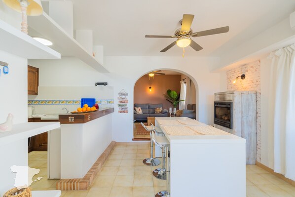 Une cuisine moderne dotée d’un îlot central, de tabourets de bar, d’un ventilateur de plafond et d’un coin repas comprenant un canapé et une table basse.