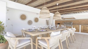 Un coin repas avec une table en bois dressée pour six personnes, entourée de chaises en osier, sous un plafond en bois agrémenté de lampes en osier suspendues.
