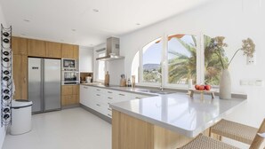 Une cuisine moderne dotée d’un grand îlot central, d’appareils électroménagers en acier inoxydable et offrant une vue sur les palmiers.
